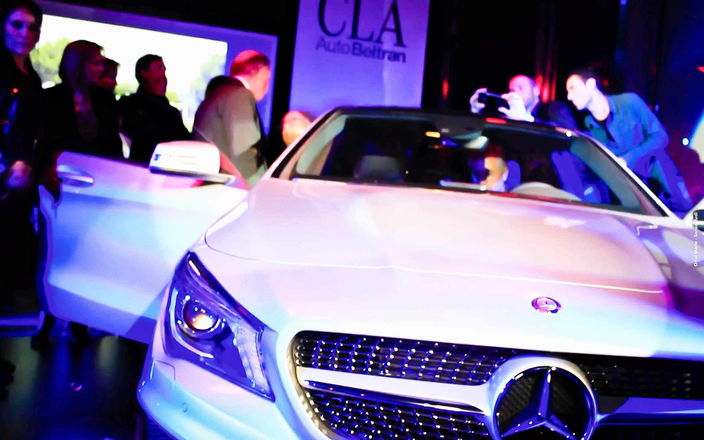 Invitados alrededor del Mercedes-Benz CLA blanco con las puertas abiertas, bajo luz azul, en la presentación de 2013