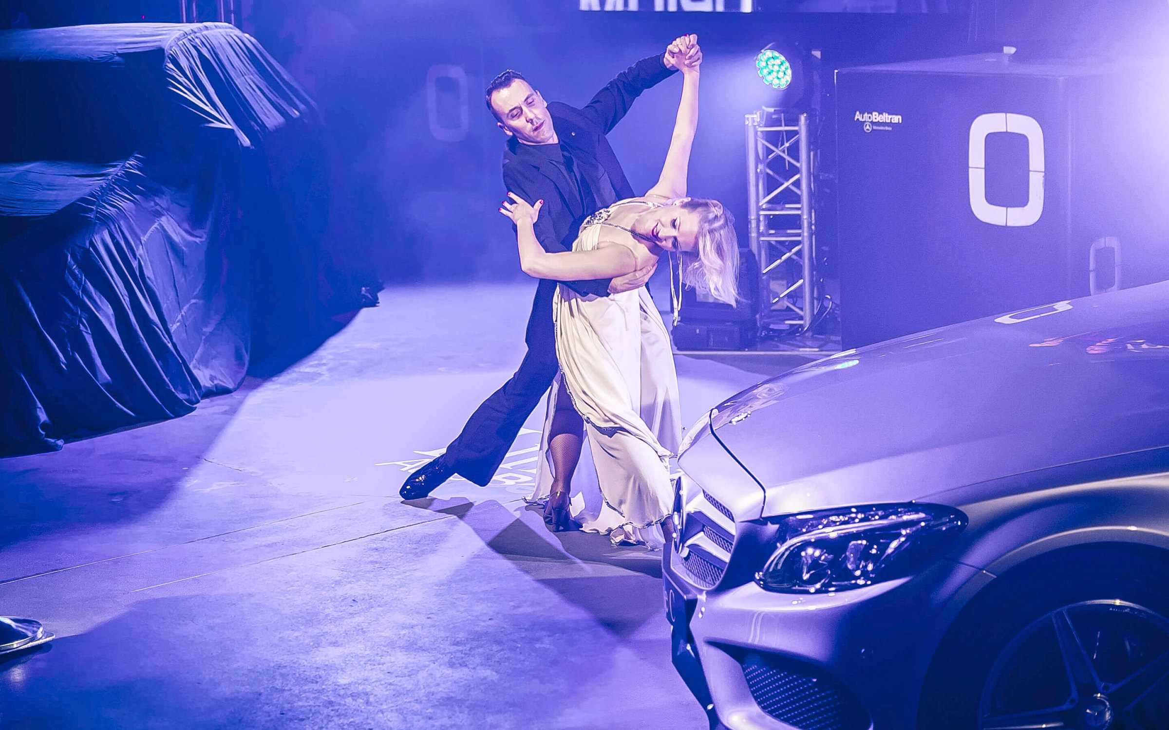 Pareja de baile sobre el escenario junto a un Mercedes-Benz, bajo luz violeta, en la presentación del GLA y la Clase C