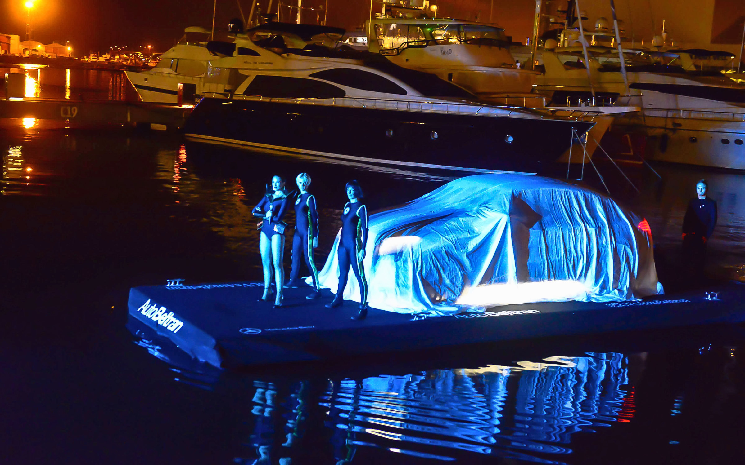 El GLE Coupé cubierto con una funda iluminada sobre una plataforma flotante en el puerto, de noche