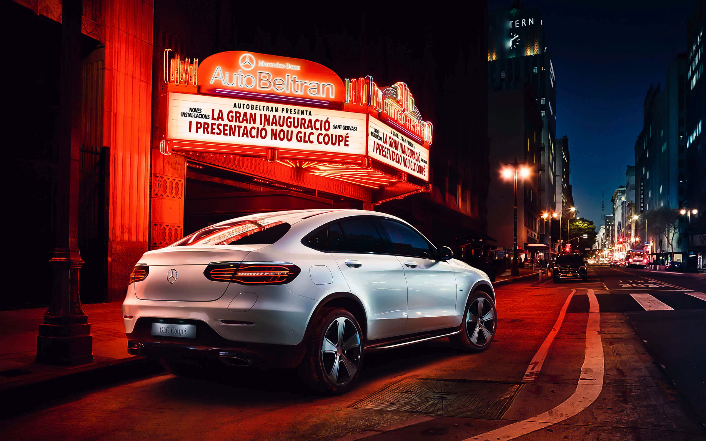 El GLC Coupé blanco frente a una marquesina de cine con el anuncio de la inauguración, en una calle de noche