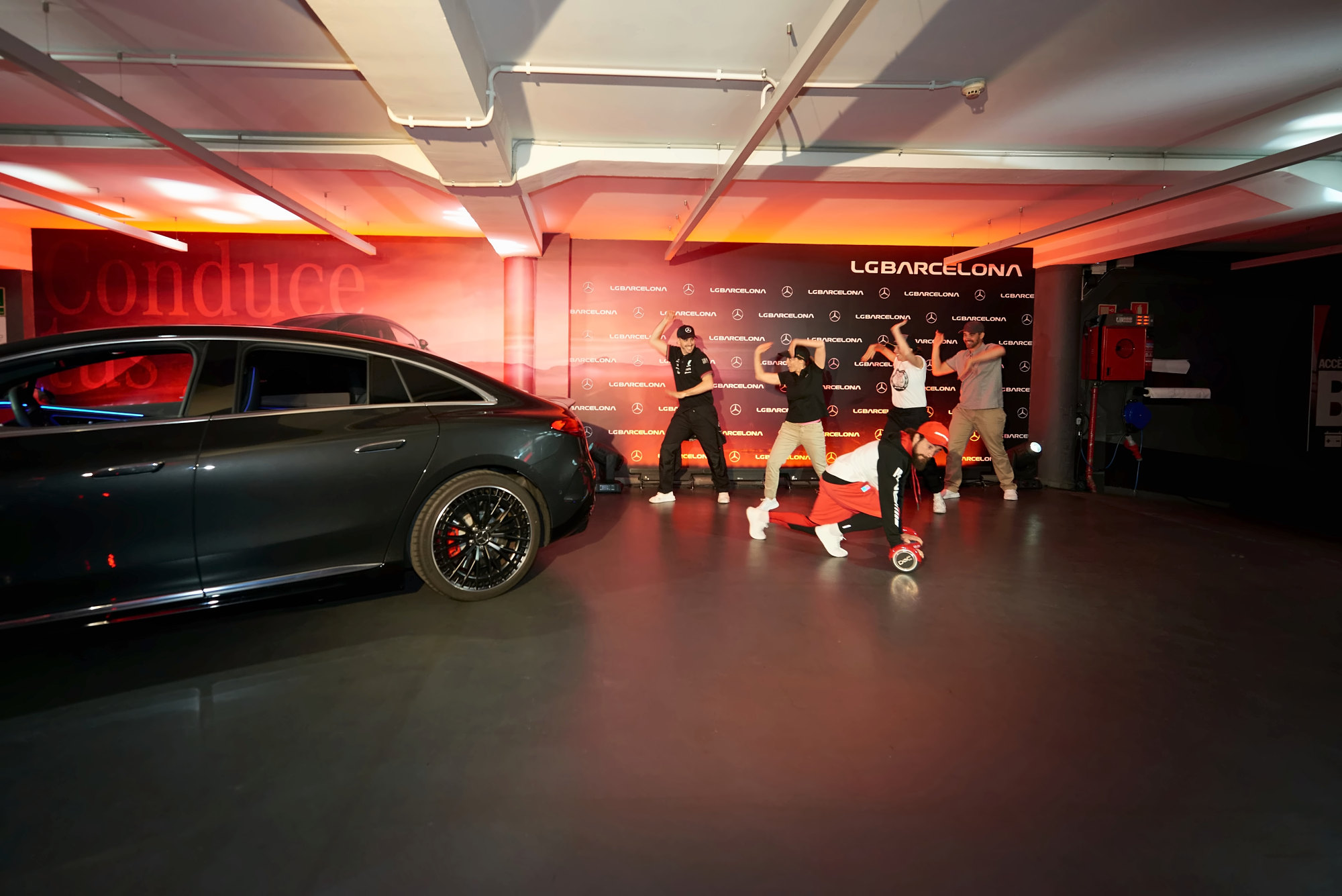 Bailarines junto a un Mercedes-Benz bajo luz roja y el photocall de LG Barcelona, en la inauguración de la Boutique