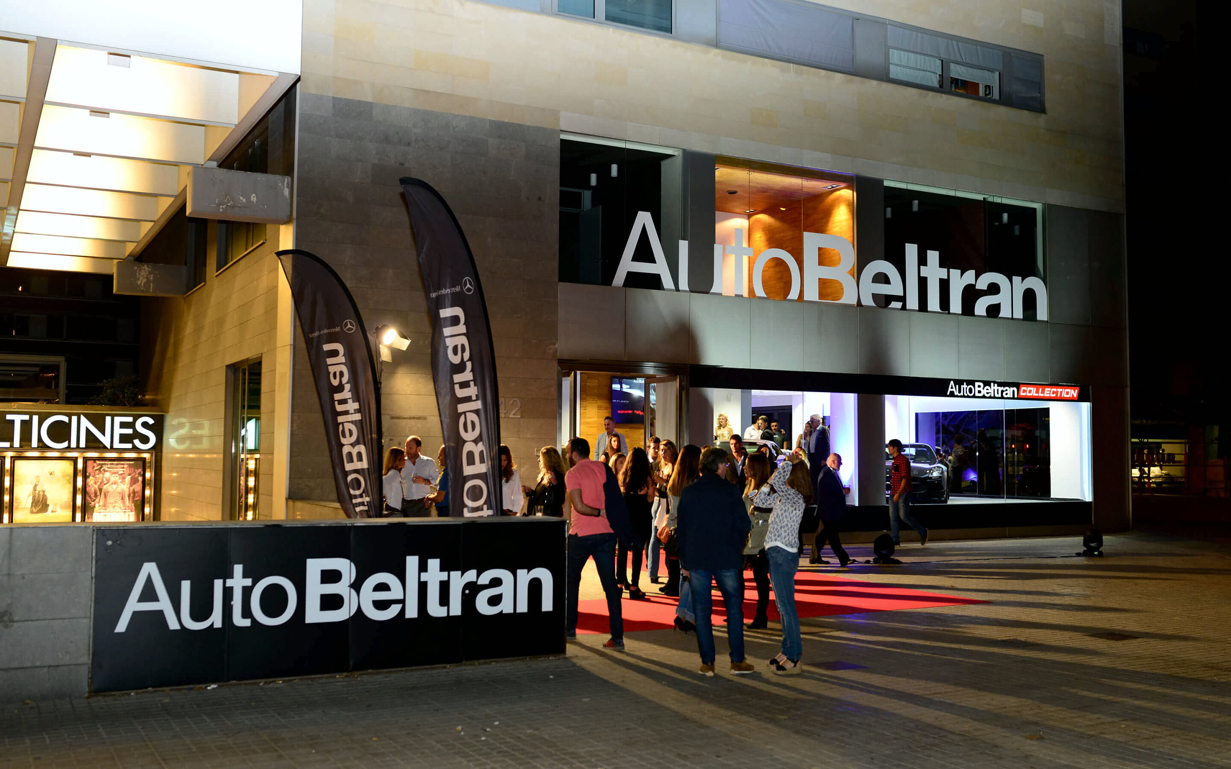 Fachada del concesionario AutoBeltrán de noche, con el rótulo encendido, alfombra roja e invitados en la entrada