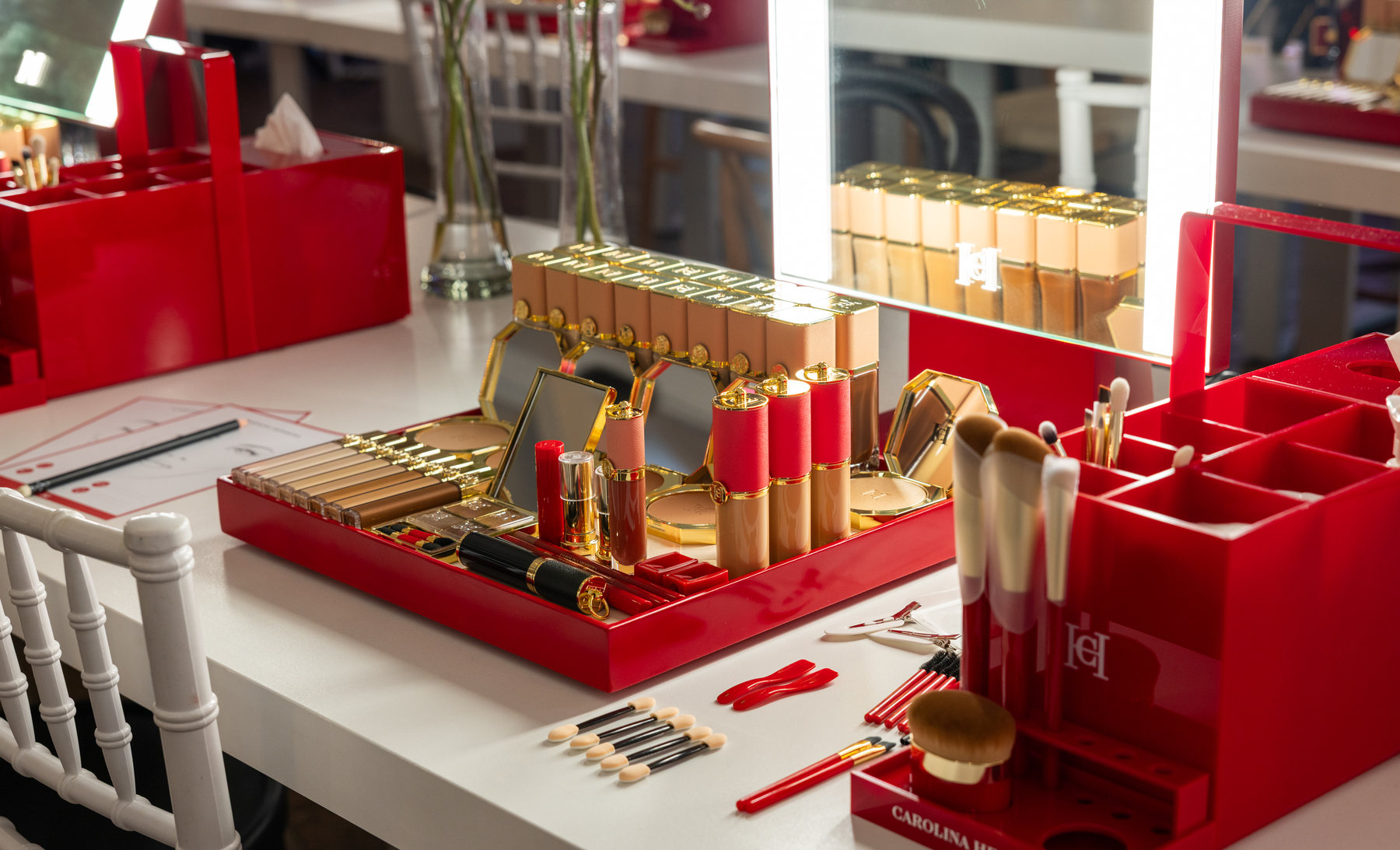Una estación de maquillaje con el estuche rojo de Carolina Herrera, bases, pinceles y el espejo de luz