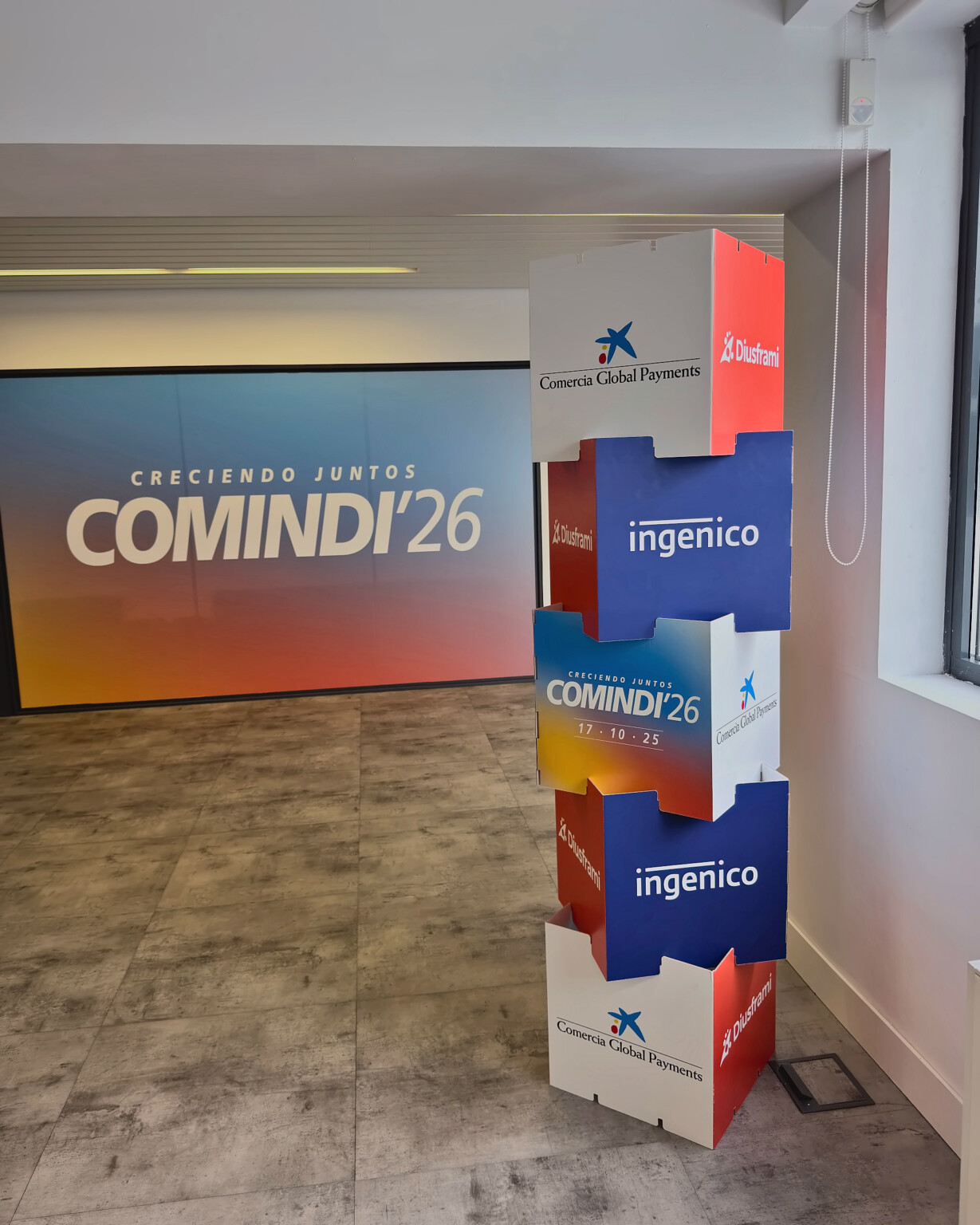 A column of printed cubes with the COMINDI'26, Comercia Global Payments, Ingenico and Diusframi brands, beside the photocall