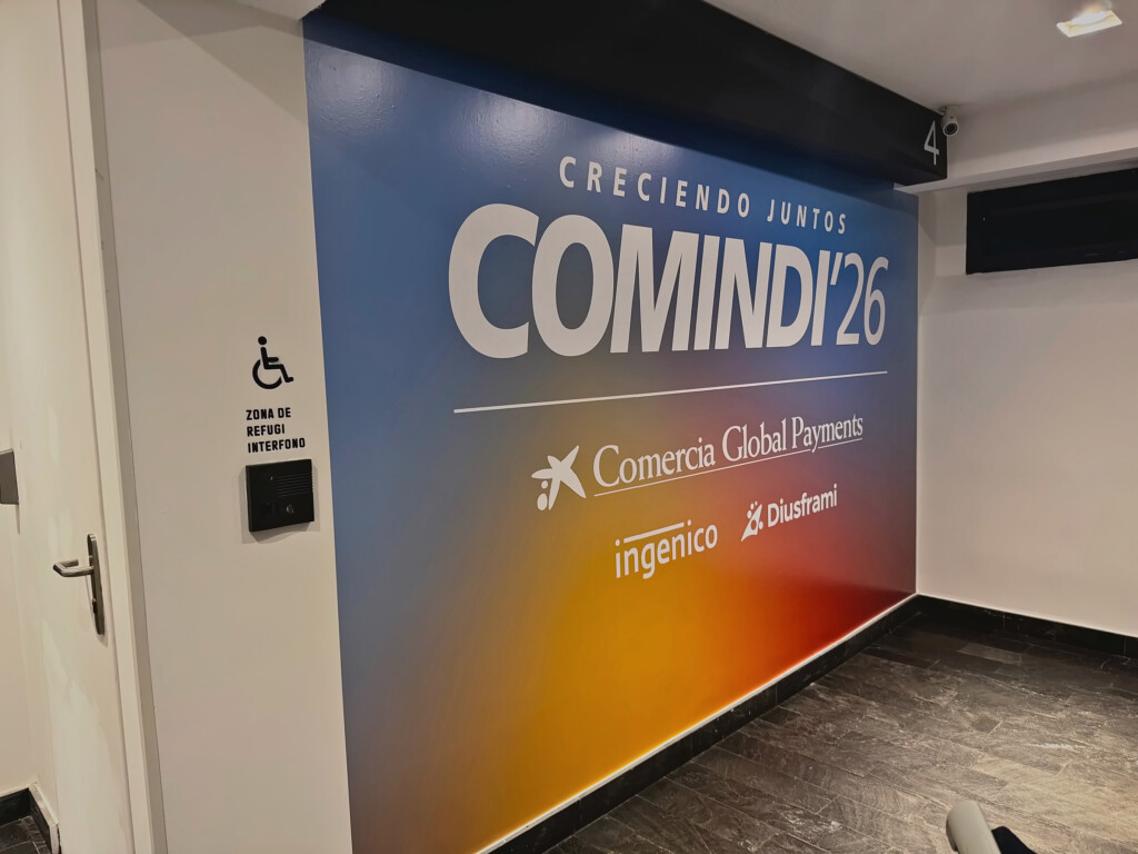 A corridor wall branded with COMINDI'26 “Creciendo juntos” (Growing together) and the Comercia Global Payments brands