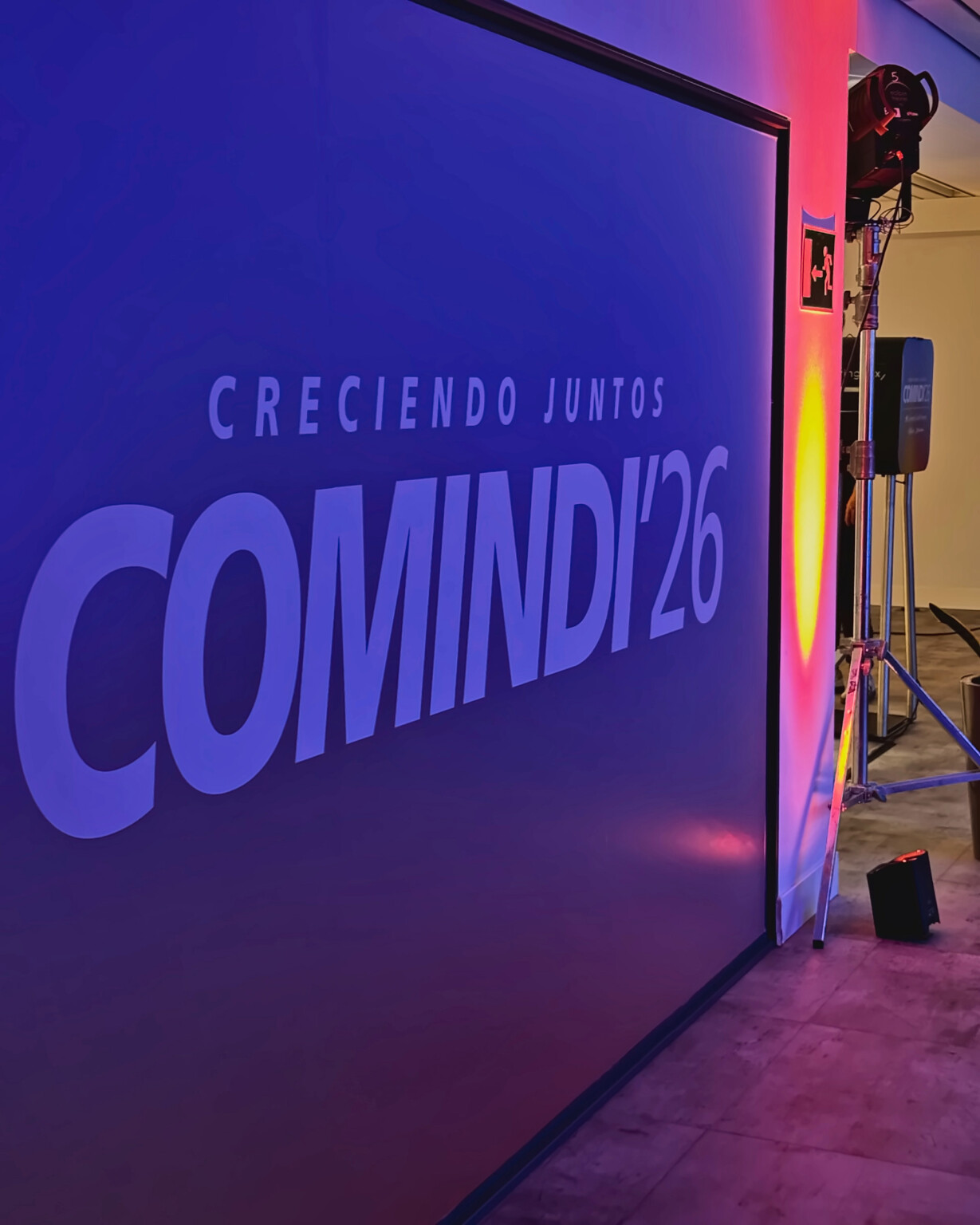 “Creciendo juntos · COMINDI'26” (Growing together) projected at large scale on a wall lit in blue