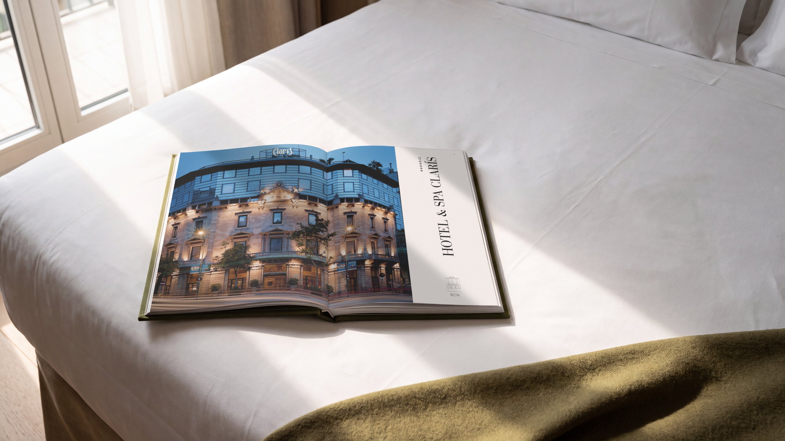 Recreación: el brandbook de Derby Hotels Collection abierto sobre la cama de una habitación, por la apertura del Hotel & Spa Claris