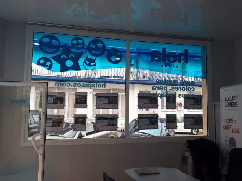 Escaparate de una oficina de Hola Pisos visto desde dentro, con los vinilos de la marca