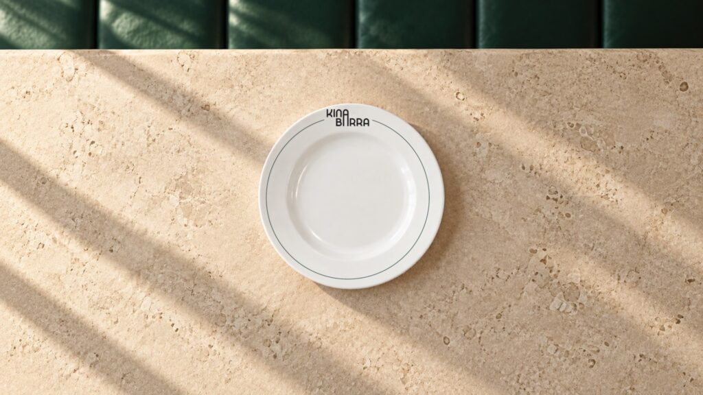 Recreación: plato de Kina Barra con el logotipo apilado y el filete verde, sobre una mesa de piedra