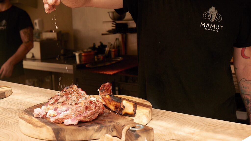 Carne servida sobre tabla en la barra de Mamut Beach Club, con el uniforme de la marca