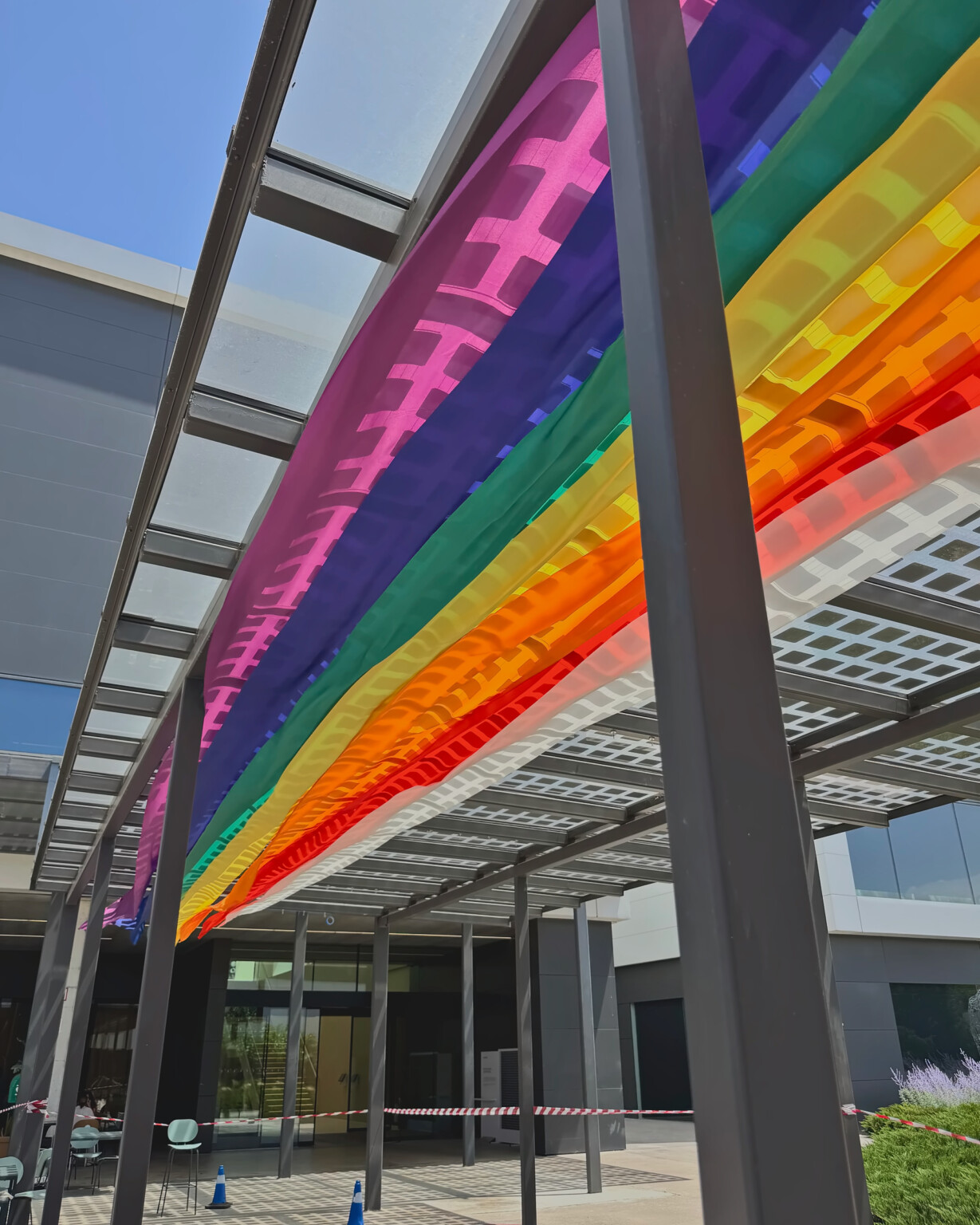 Telas del Orgullo en diagonal bajo la pérgola, vistas desde abajo junto al edificio de Mango