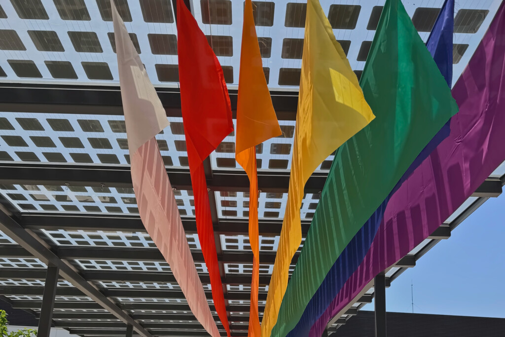 Telas con los colores del Orgullo colgadas en abanico bajo la pérgola de placas solares de la sede central de Mango