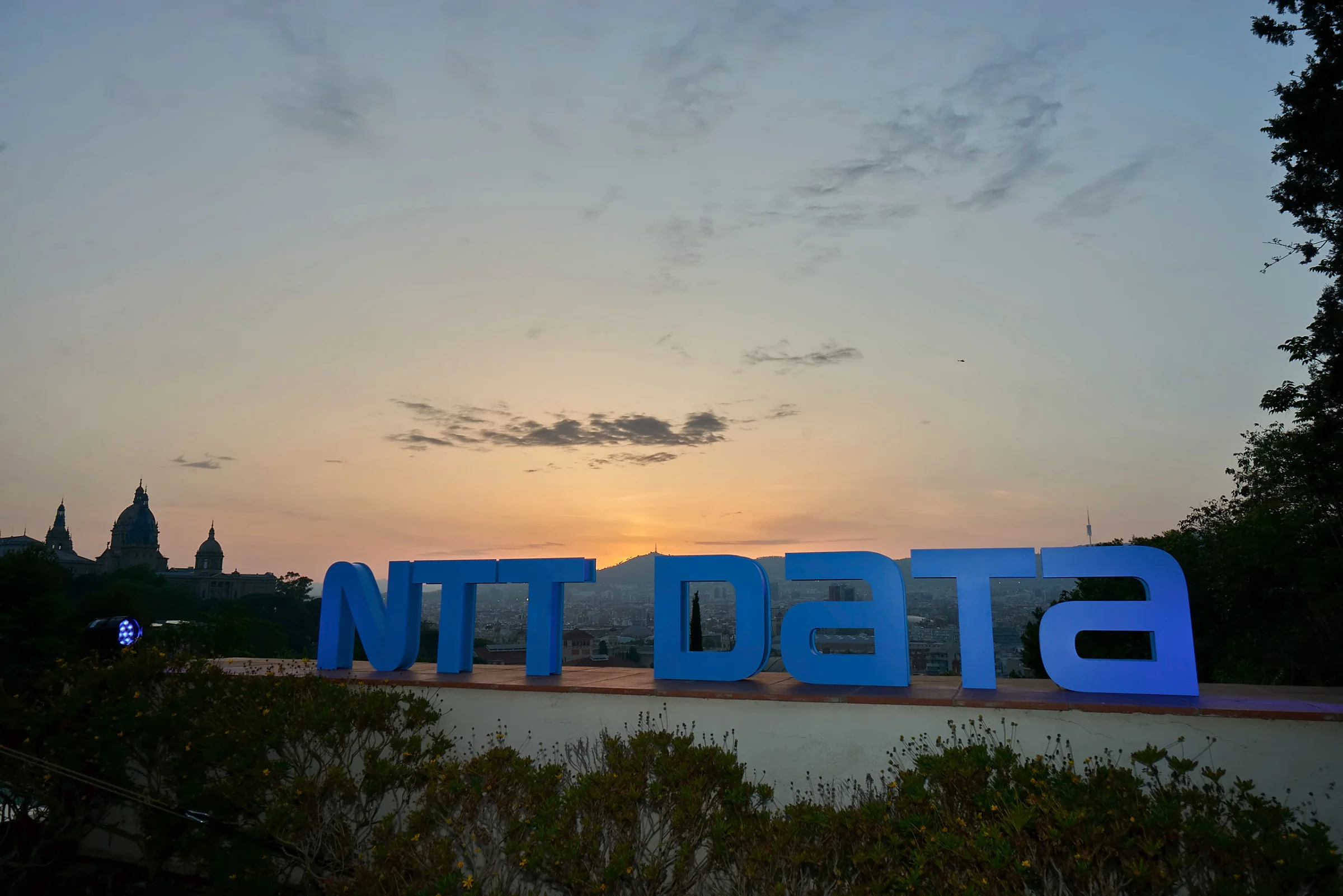Letras de NTT DATA al atardecer en la terraza de la Fundació Joan Miró, con el MNAC al fondo