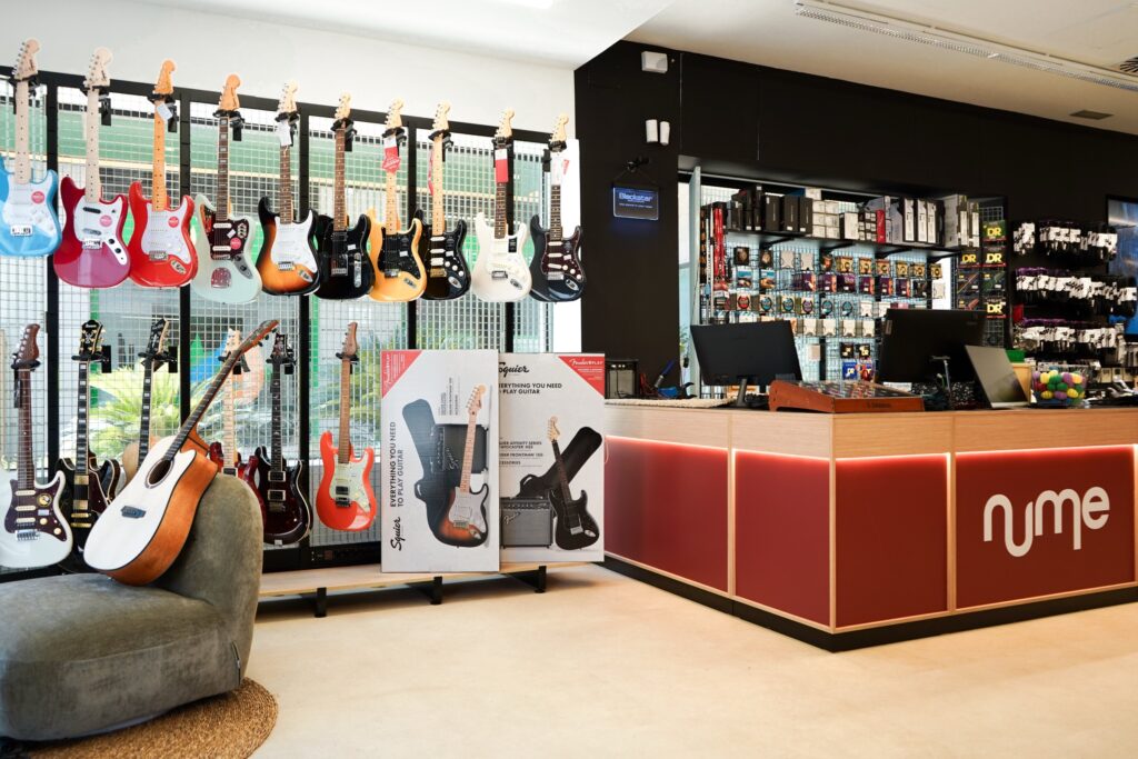 Mostrador de la tienda nUme de Sevilla en color clay con el logotipo, junto a la pared de guitarras eléctricas