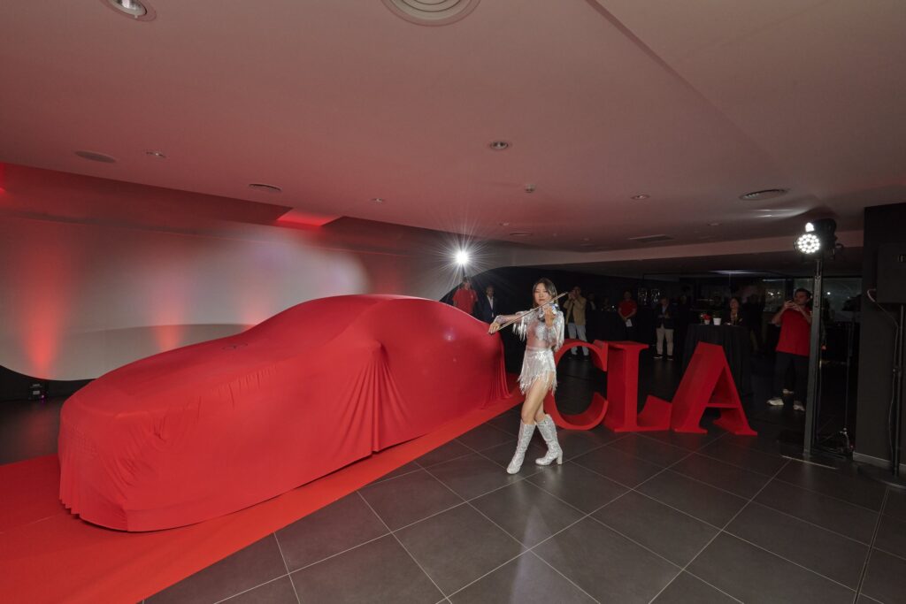 El nuevo CLA cubierto con una funda roja sobre la alfombra, con una violinista y las letras CLA, antes del desvelado