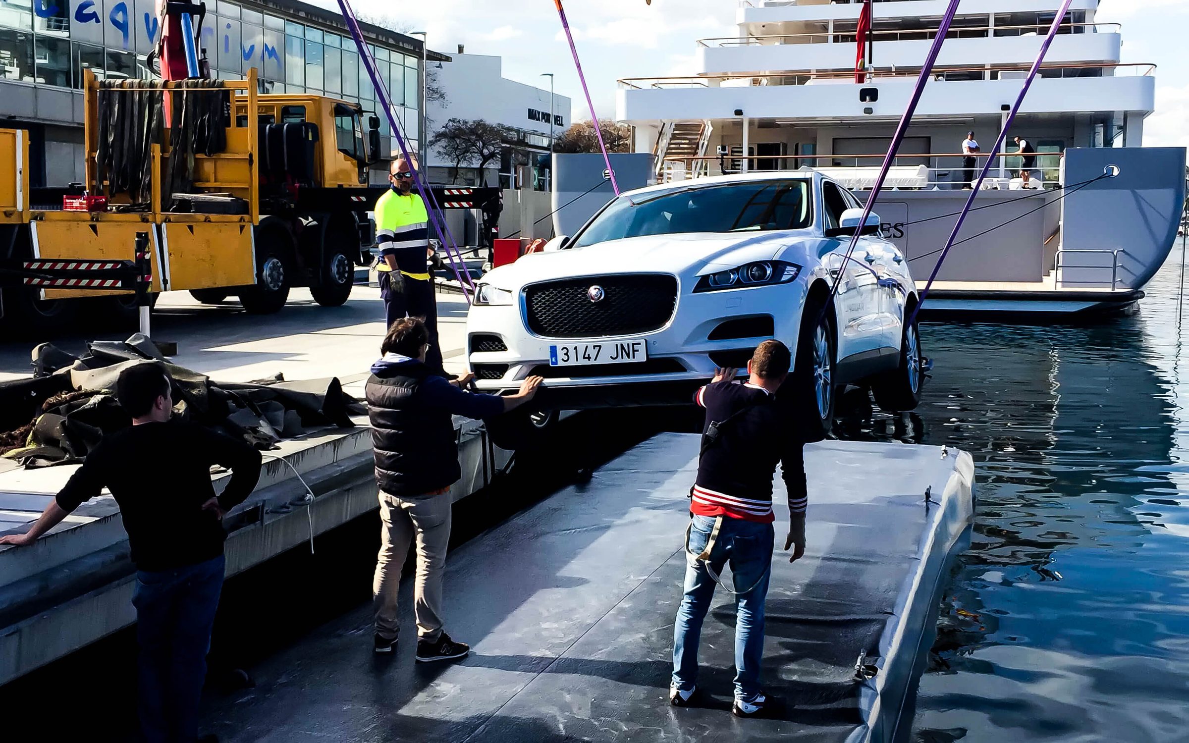 De día, una grúa baja el Jaguar F-Pace a la plataforma flotante en el muelle del Port Vell