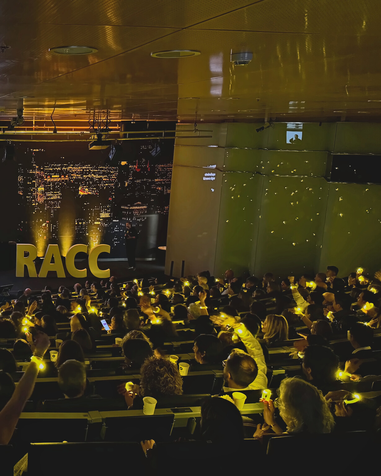 Attendees holding yellow lights aloft beside the RACC letters during the 2026 sales meeting