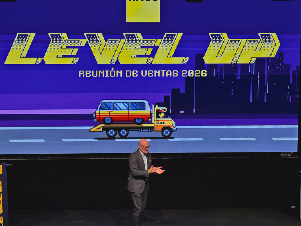 A speaker in front of the big Level Up screen at the 2026 sales meeting, with the pixelated recovery truck