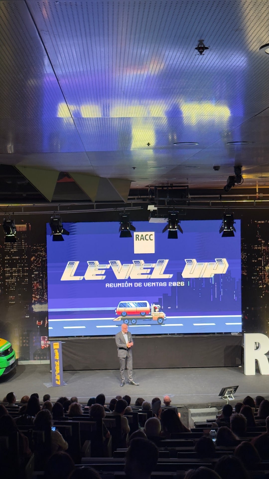 Vista vertical del escenario de la reunión de ventas 2026 del RACC con Level Up en pantalla y el público