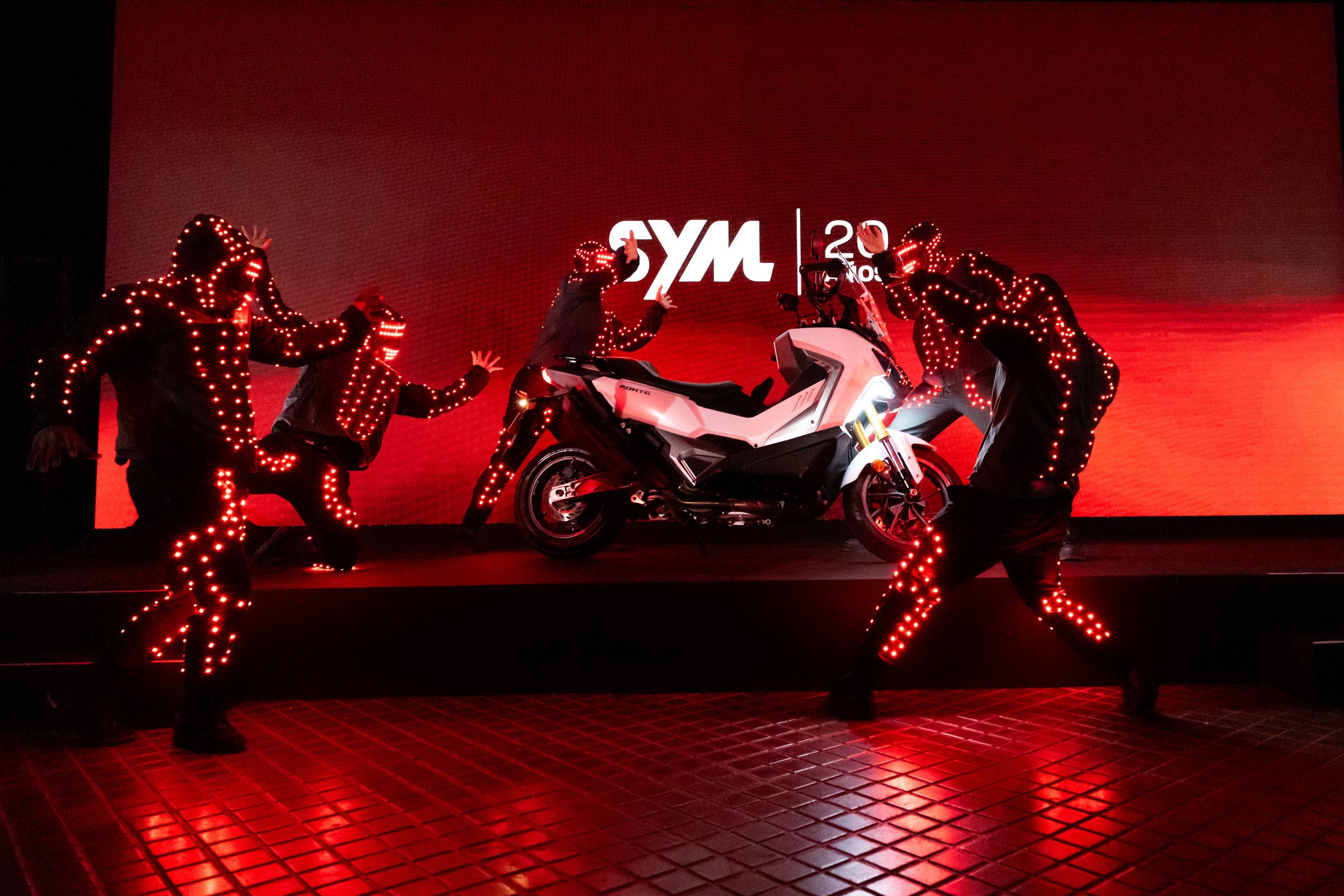 Bailarines de luz y un ADX-TG sobre el escenario rojo del 20 aniversario