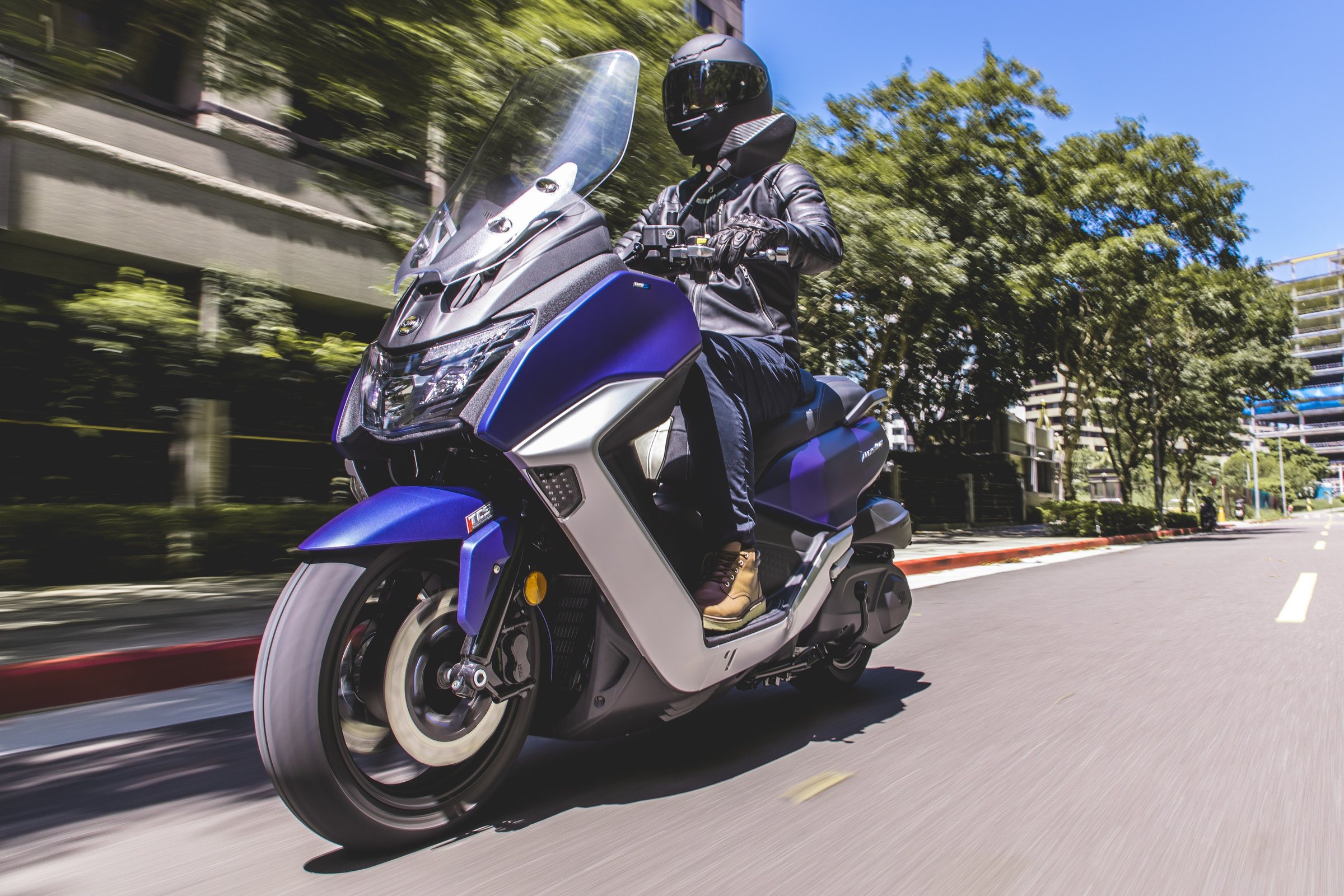 Maxsym 400 azul en marcha junto a una arboleda