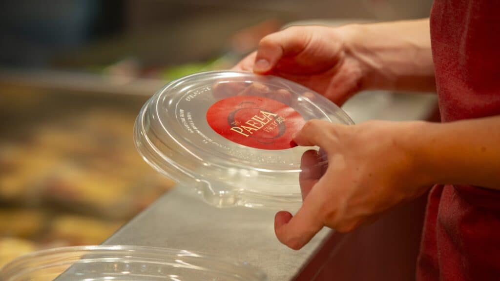 Envase para llevar de The Paella Factory con la etiqueta redonda de la marca