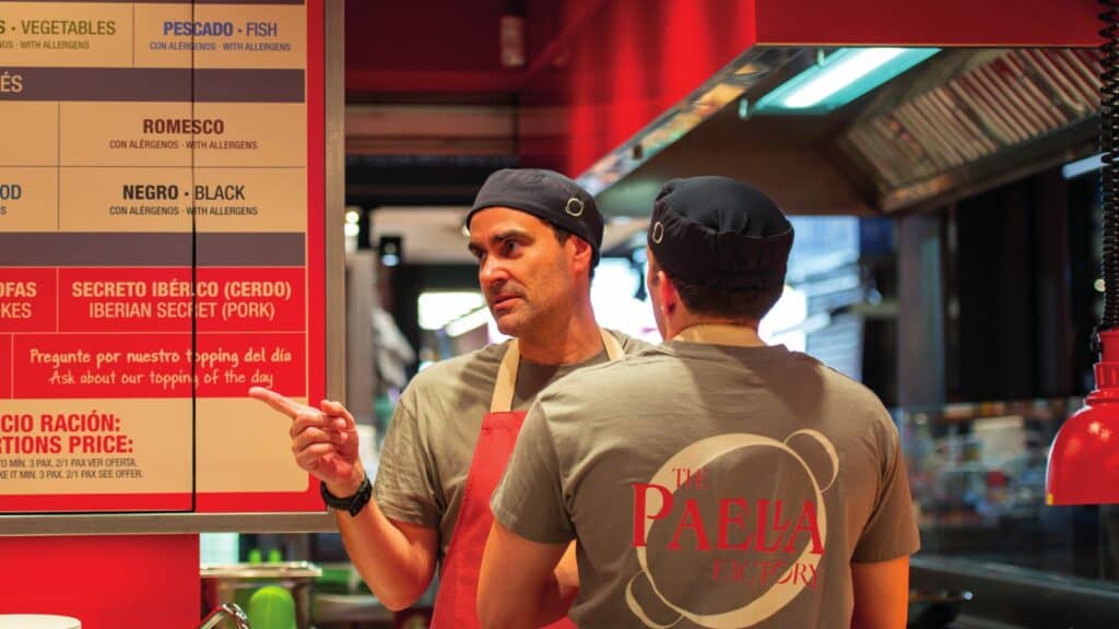 Equipo de The Paella Factory con los uniformes de la marca frente a la carta