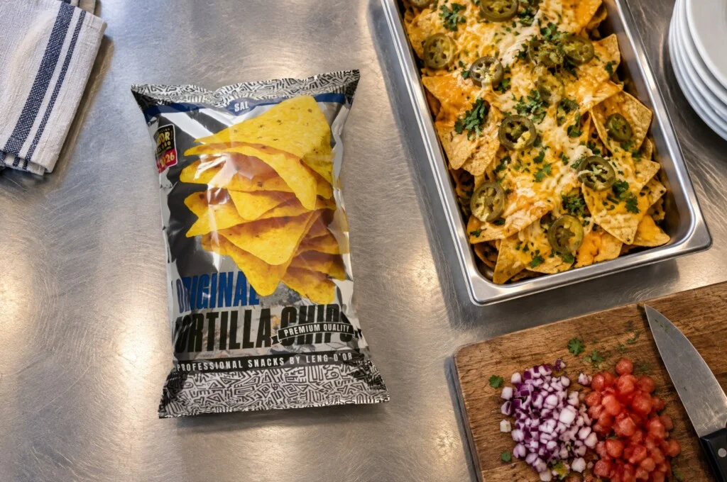 Recreación: bolsa de Original Tortilla Chips de Leng-d’Or en la cocina de un restaurante, junto a una bandeja de nachos gratinados