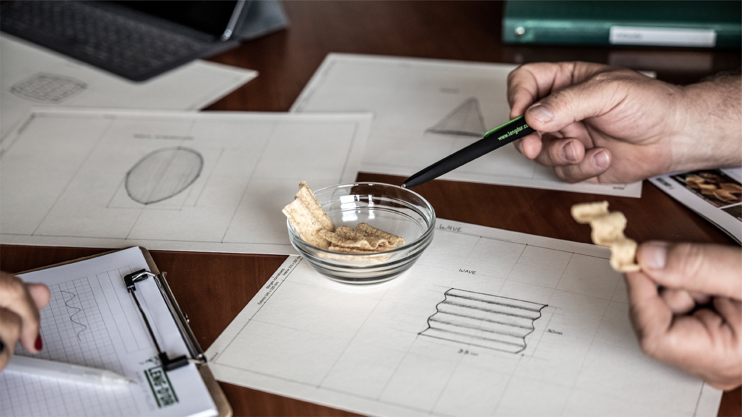 Bocetos de formas de snack sobre la mesa, con una muestra en la mano y un cuenco de snacks