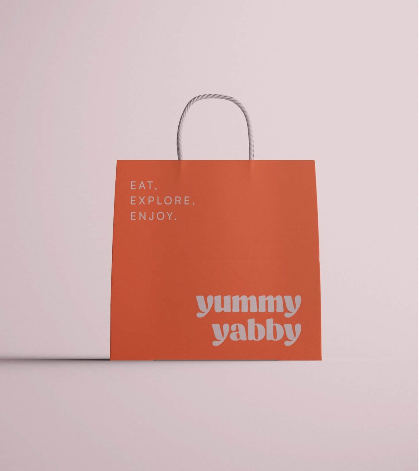 Bolsa de papel naranja de Yummy Yabby con el lema Eat. Explore. Enjoy.