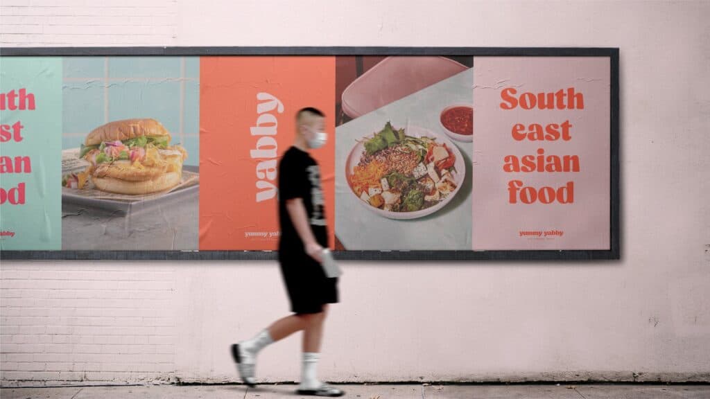 Carteles de Yummy Yabby en una pared rosa con un peatón delante
