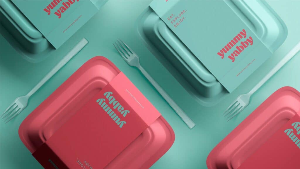 Envases para llevar de Yummy Yabby en rosa y turquesa, con fundas de la marca y cubiertos