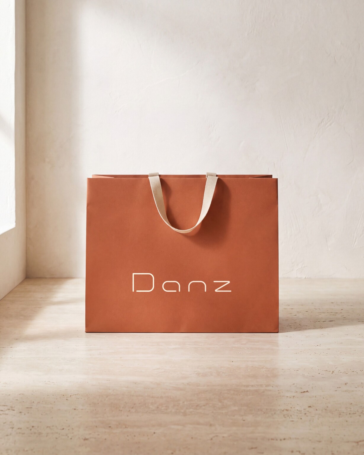 Recreación: bolsa de papel terracota con el logotipo de DANZ Barcelona en blanco, sobre suelo de travertino