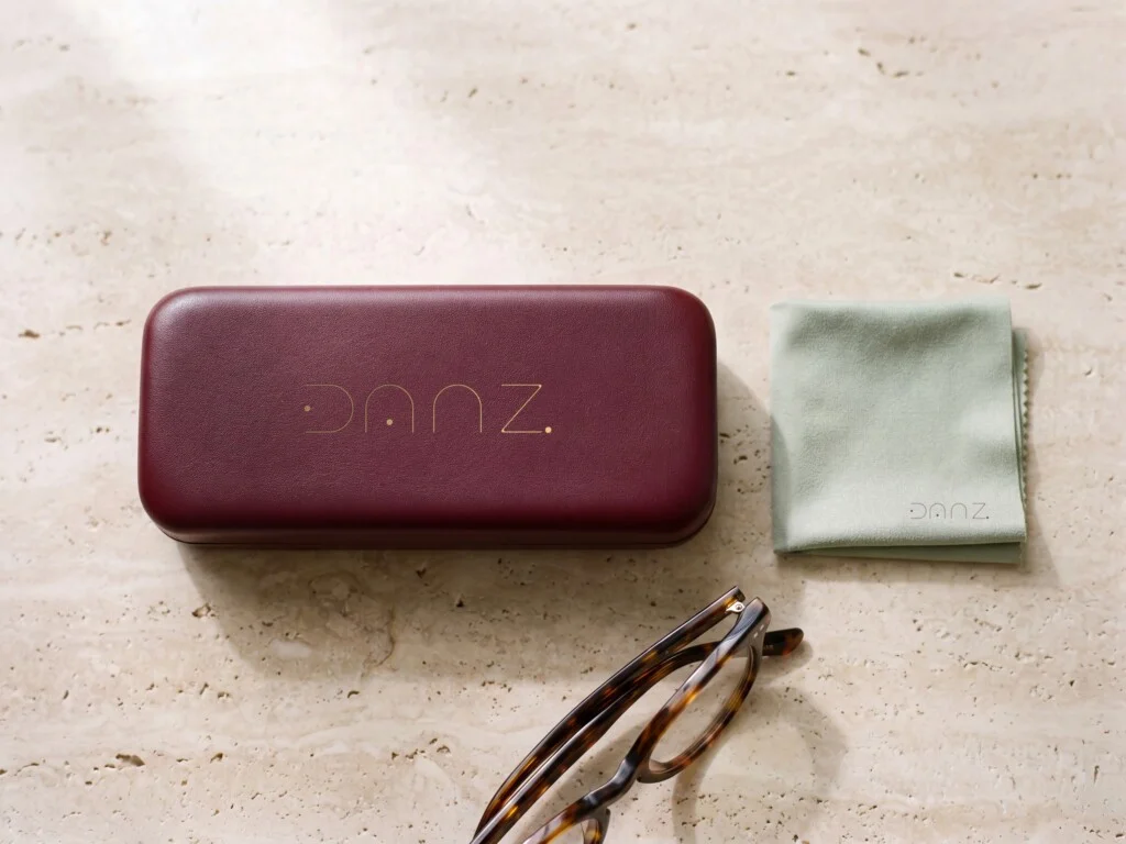 Recreación: estuche de piel burdeos con el logotipo de DANZ Barcelona estampado en oro y gamuza verde piedra sobre travertino