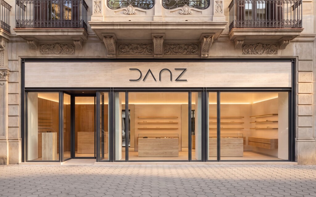 Recreación: fachada de una tienda de DANZ Barcelona en un edificio modernista del Eixample, con el logotipo en letras de metal grafito sobre travertino