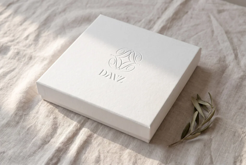 Recreación: caja blanca con el símbolo y el logotipo de la línea «Escultura y mar» de DANZ en gofrado seco
