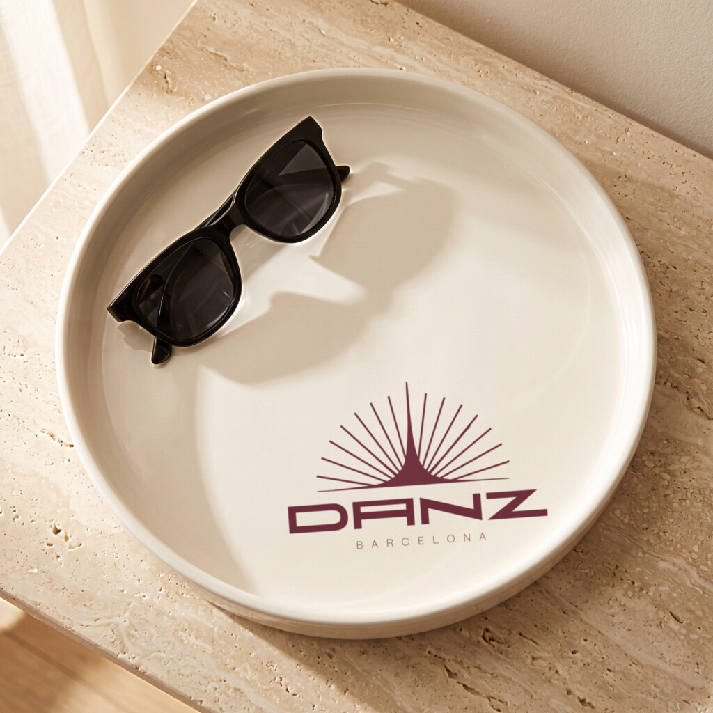 Recreación: bandeja de cerámica con el logotipo del sol «El último destello» de DANZ en burdeos y unas gafas de sol
