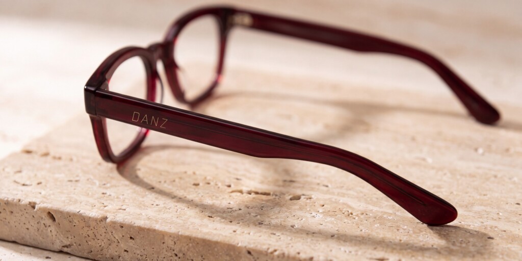 Recreación: gafas de acetato burdeos sobre travertino con el logotipo de DANZ Barcelona impreso en oro en la varilla