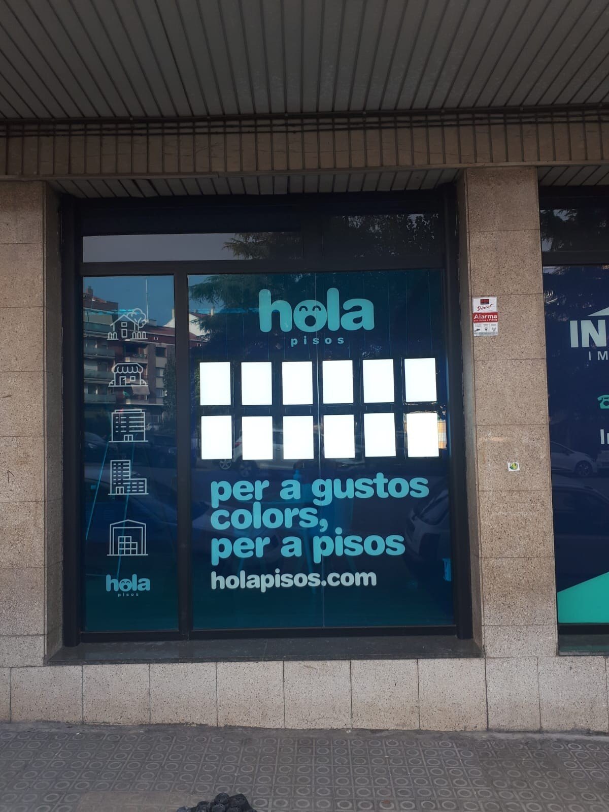 The front of a Hola Pisos office with the vinyls in Catalan: “per a gustos colors, per a pisos hola pisos”