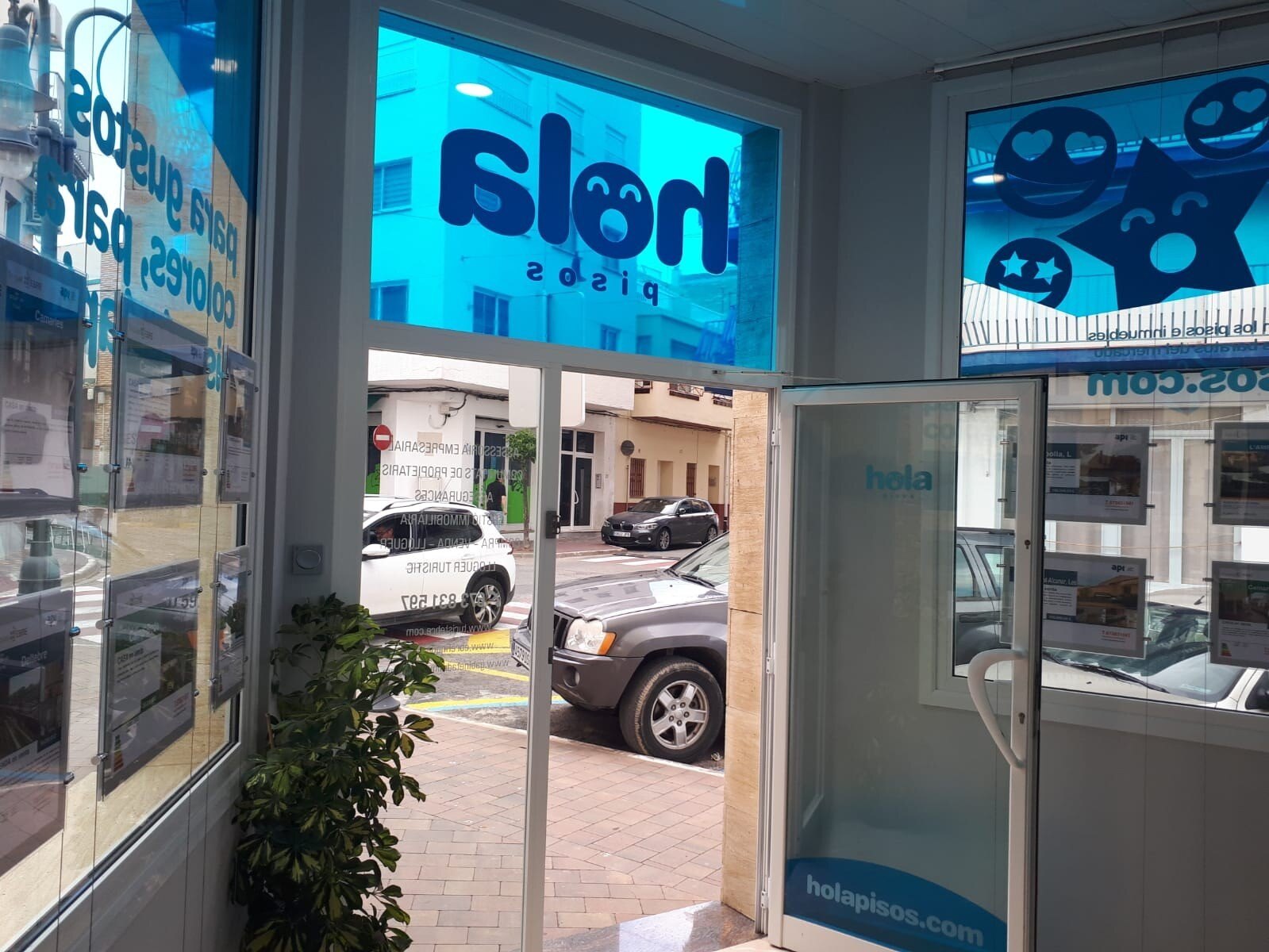 The entrance to a Hola Pisos office seen from inside, with the logo on the glass