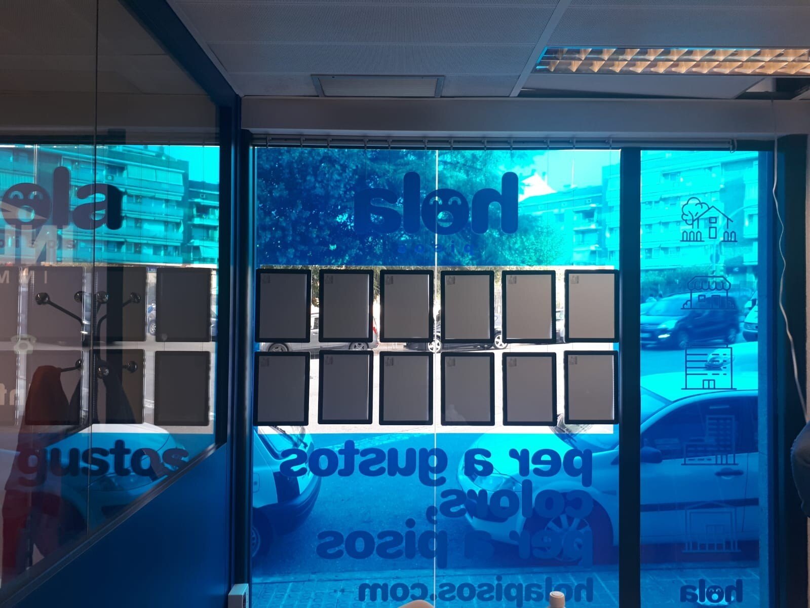 The window of a Hola Pisos office from inside, with the blue vinyls and the slogan in Catalan