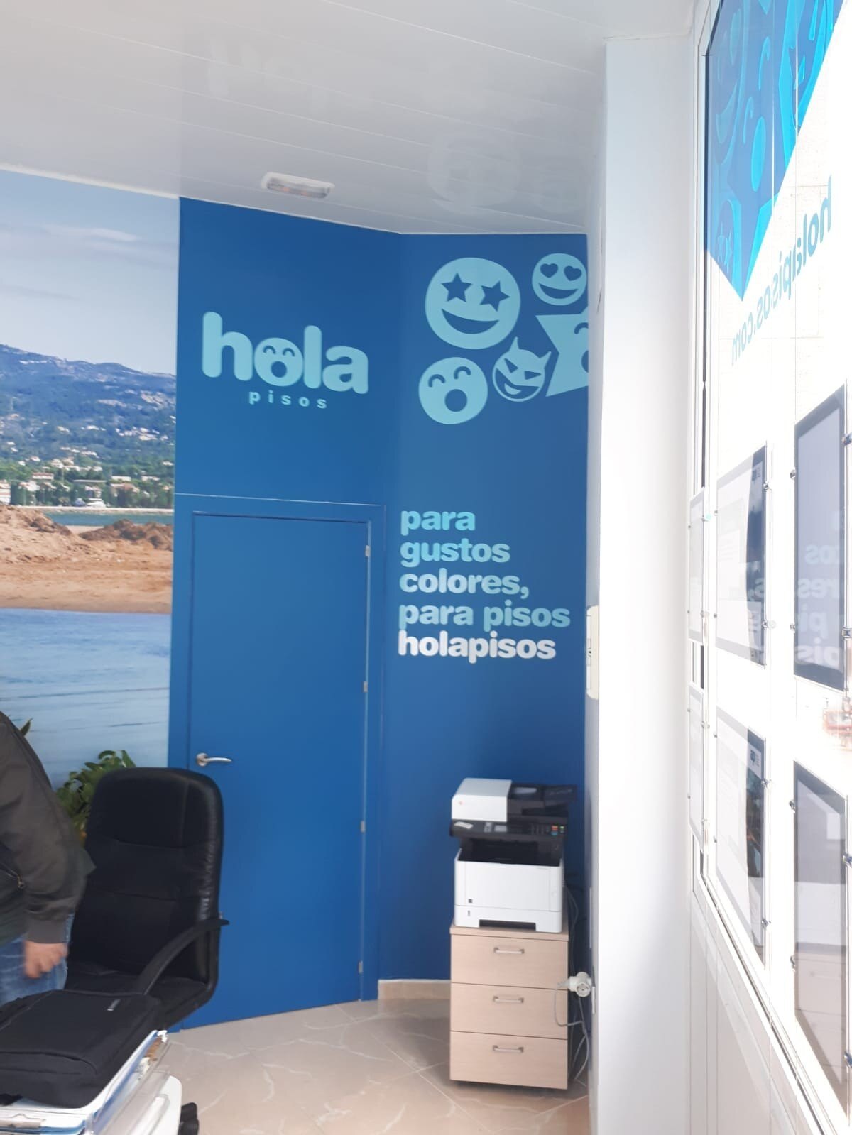 Inside a Hola Pisos office, with a blue wall bearing the logo and the faces