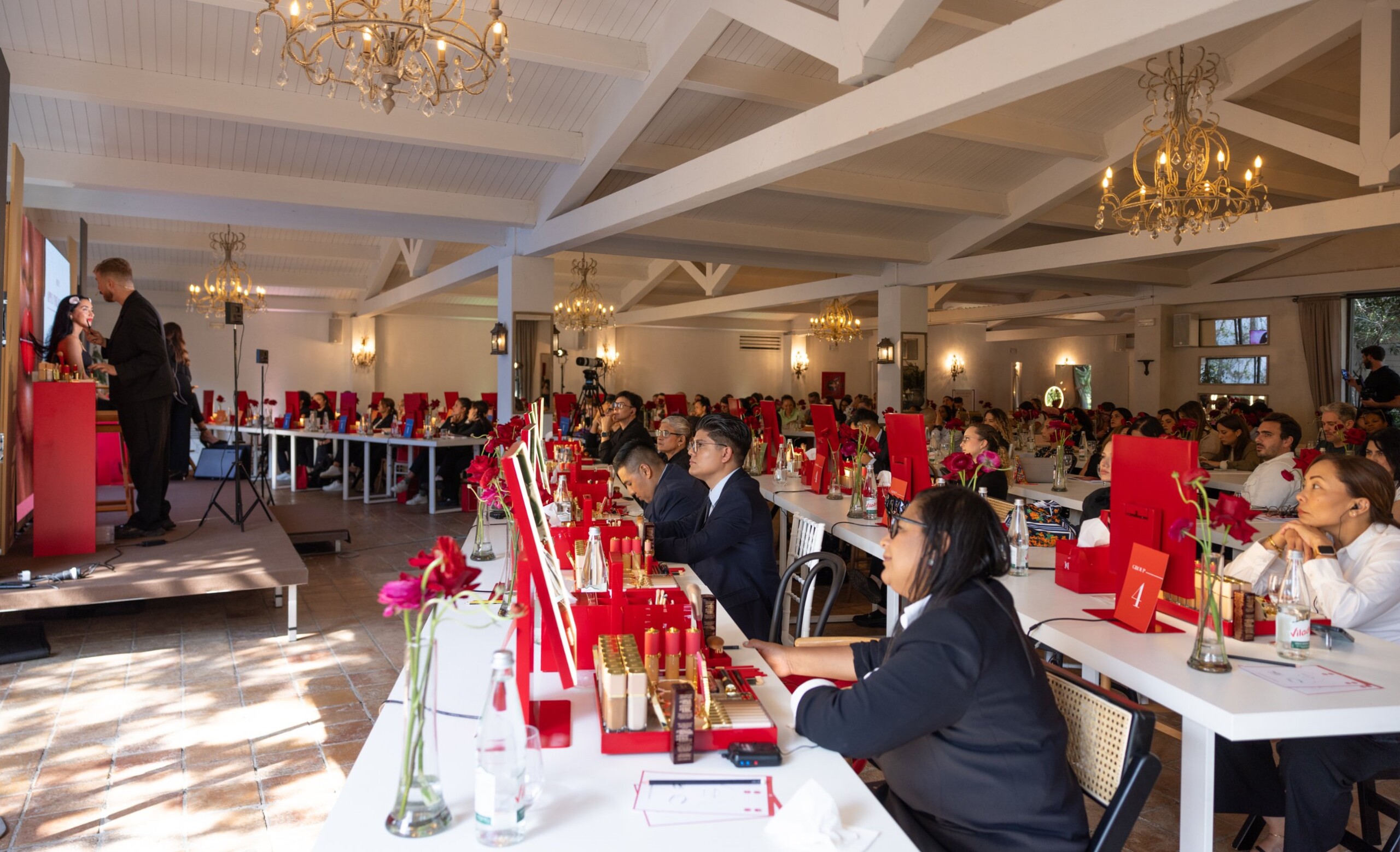 Carolina Herrera Seminar 2026: demostración de maquillaje en el escenario ante la sala llena, con puestos de producto en rojo