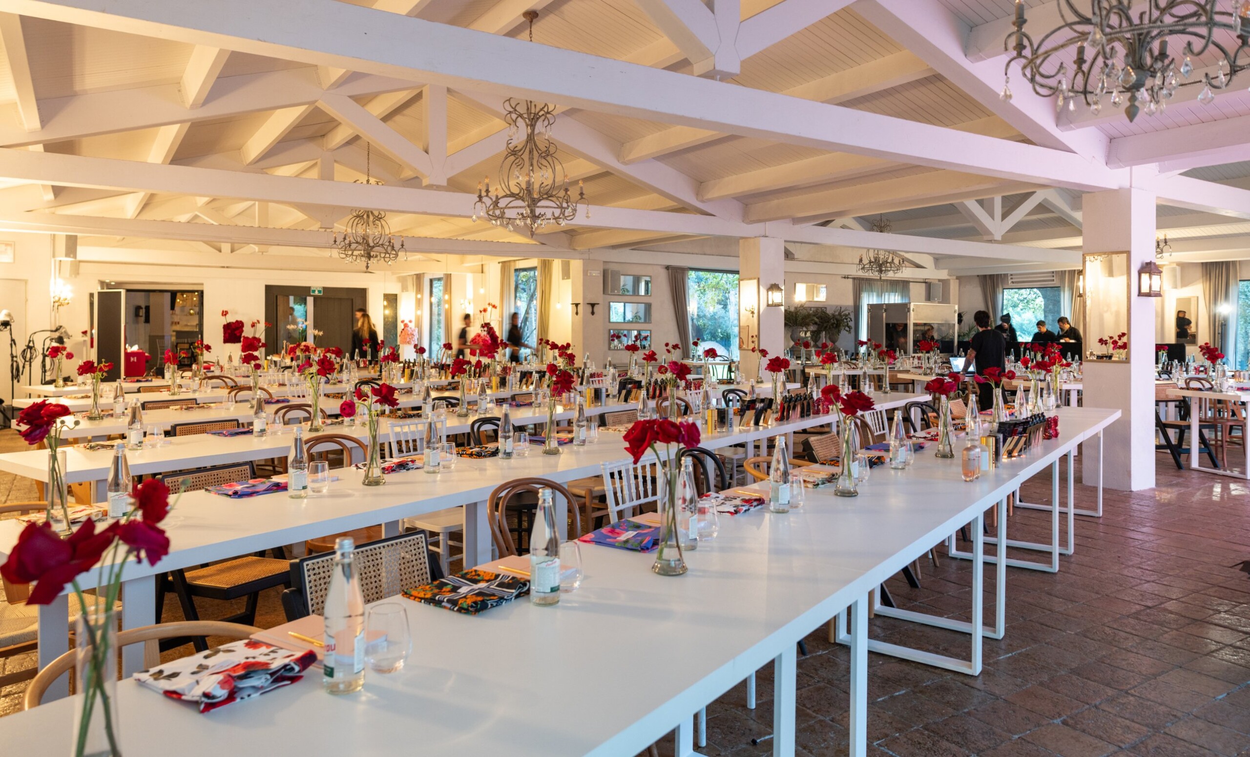 Carolina Herrera Seminar 2026: sala montada con mesas largas, flores rojas y producto de la marca