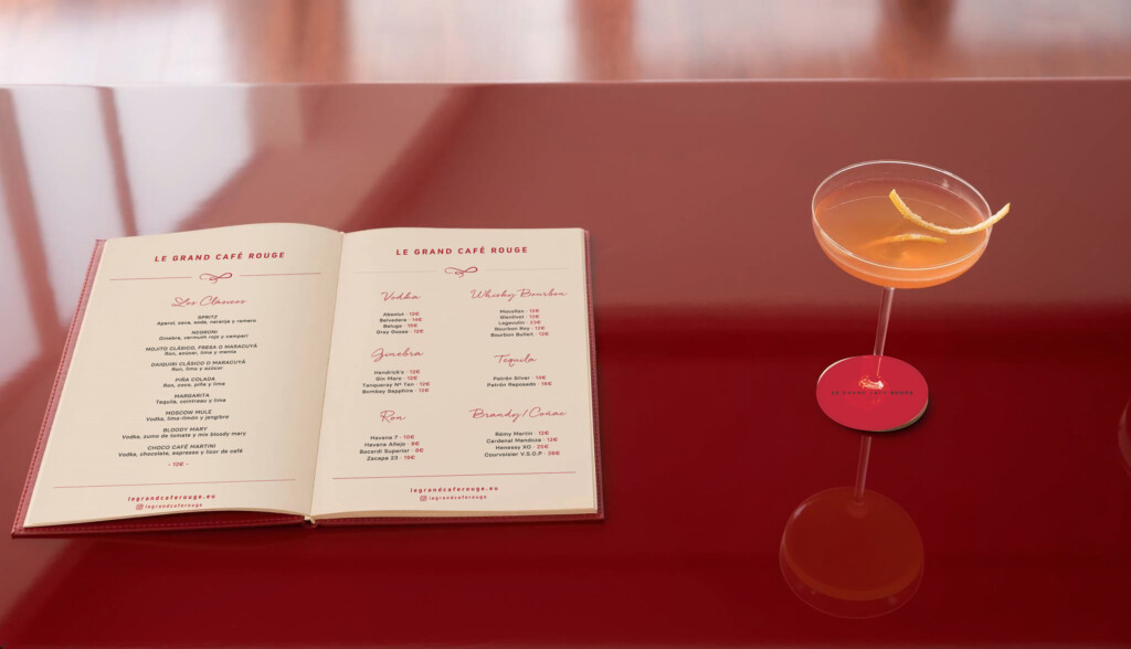 Recreación: carta de cócteles de Le Grand Café Rouge abierta sobre una barra roja junto a una copa sobre el posavasos