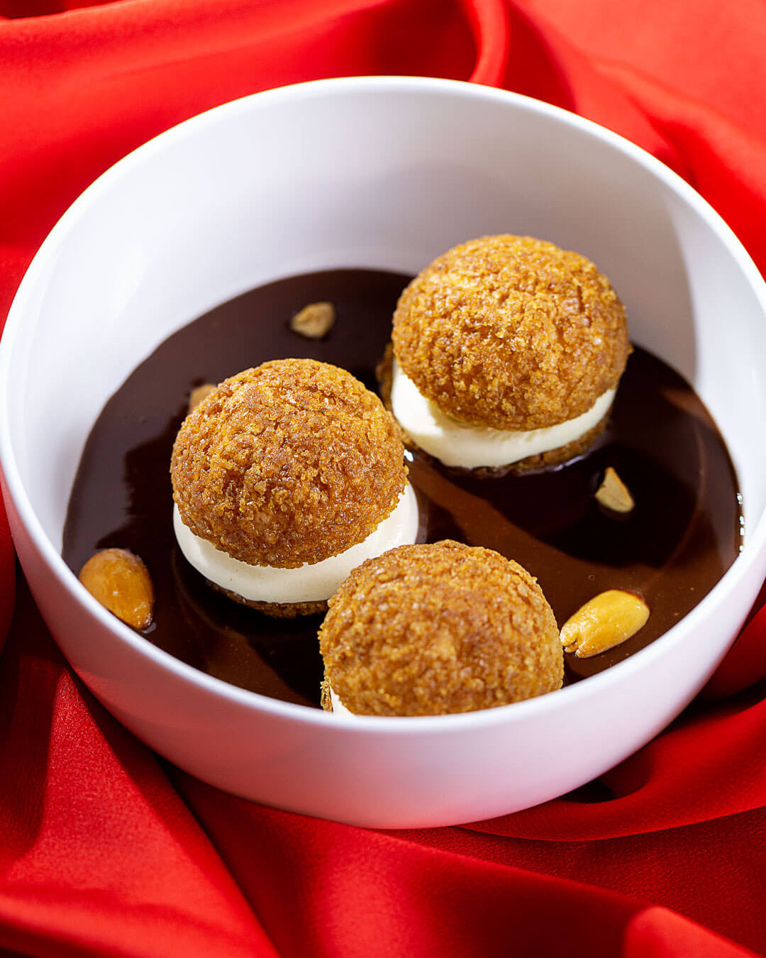 Profiteroles con salsa de chocolate en un bol blanco sobre tela roja, de la sesión de fotografía de Le Grand Café Rouge