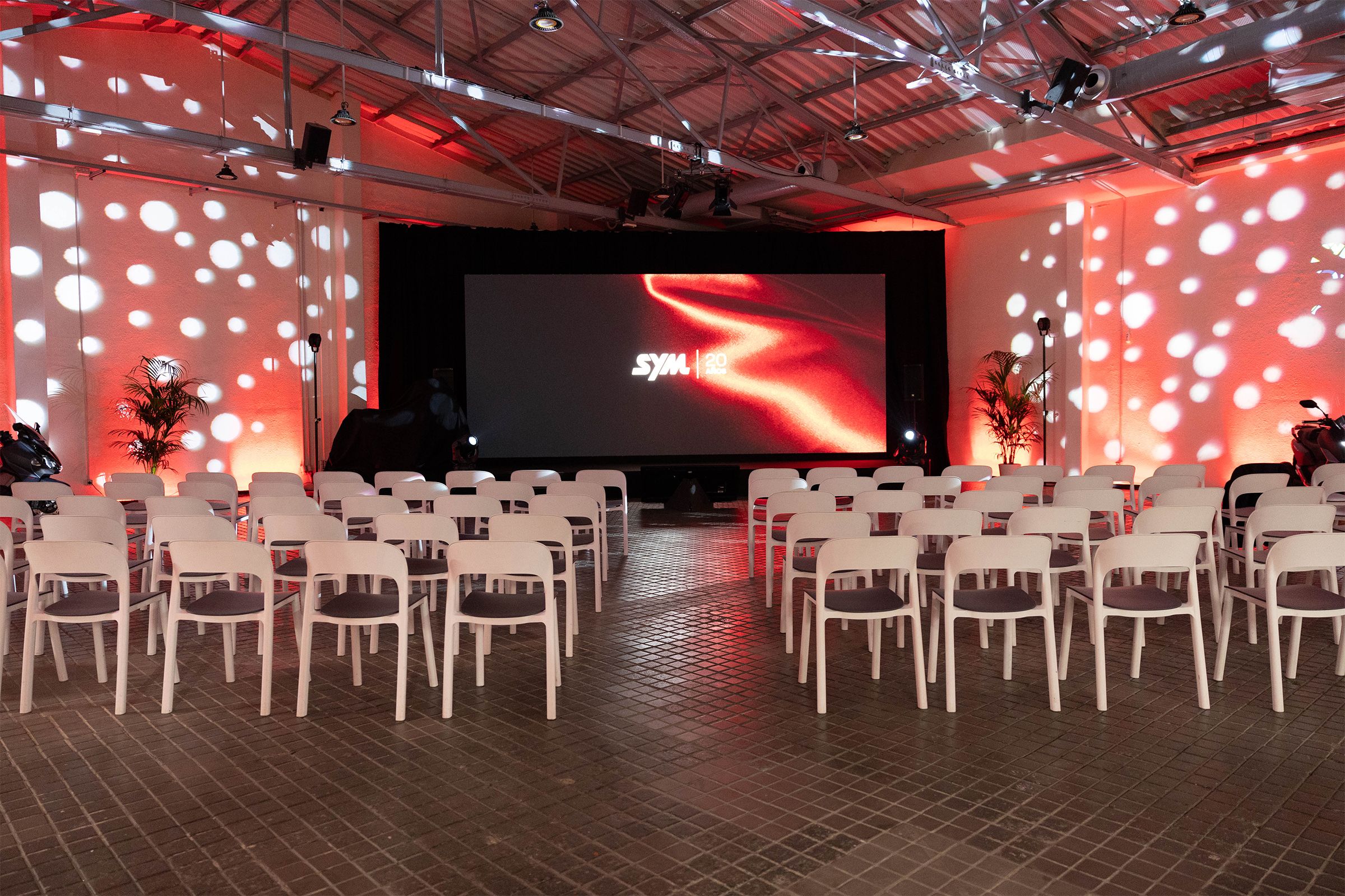 Sala del 20 aniversario de SYM España con la pantalla LED encendida y las sillas preparadas