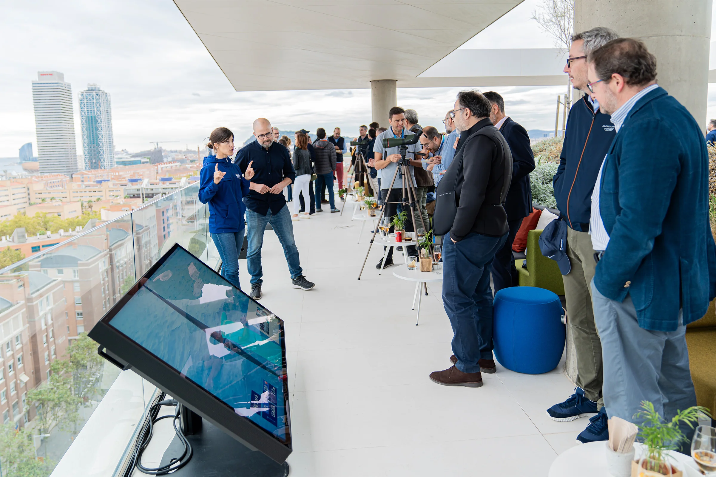 Invitados de NTT DATA en la terraza frente al mar durante la Copa América de vela 2024, con pantallas táctiles y telescopios