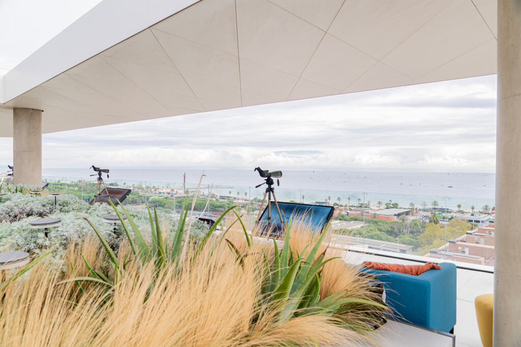 Terraza del encuentro de NTT DATA con vegetación, telescopios y pantallas frente al mar de Barcelona