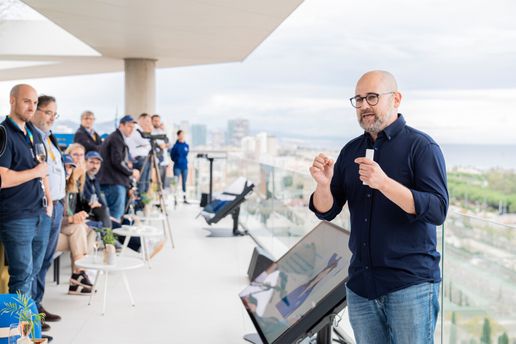 Presentador del encuentro de NTT DATA hablando a los invitados en la terraza, con Barcelona al fondo